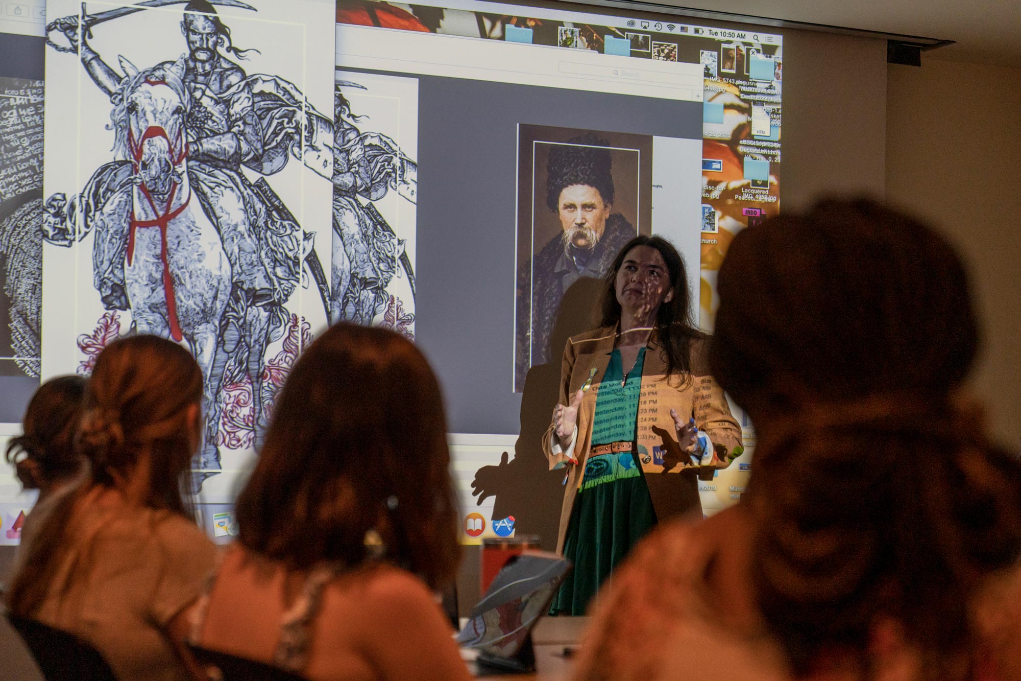 A woman stands at the front of a classroom presenting on a war-related art piece