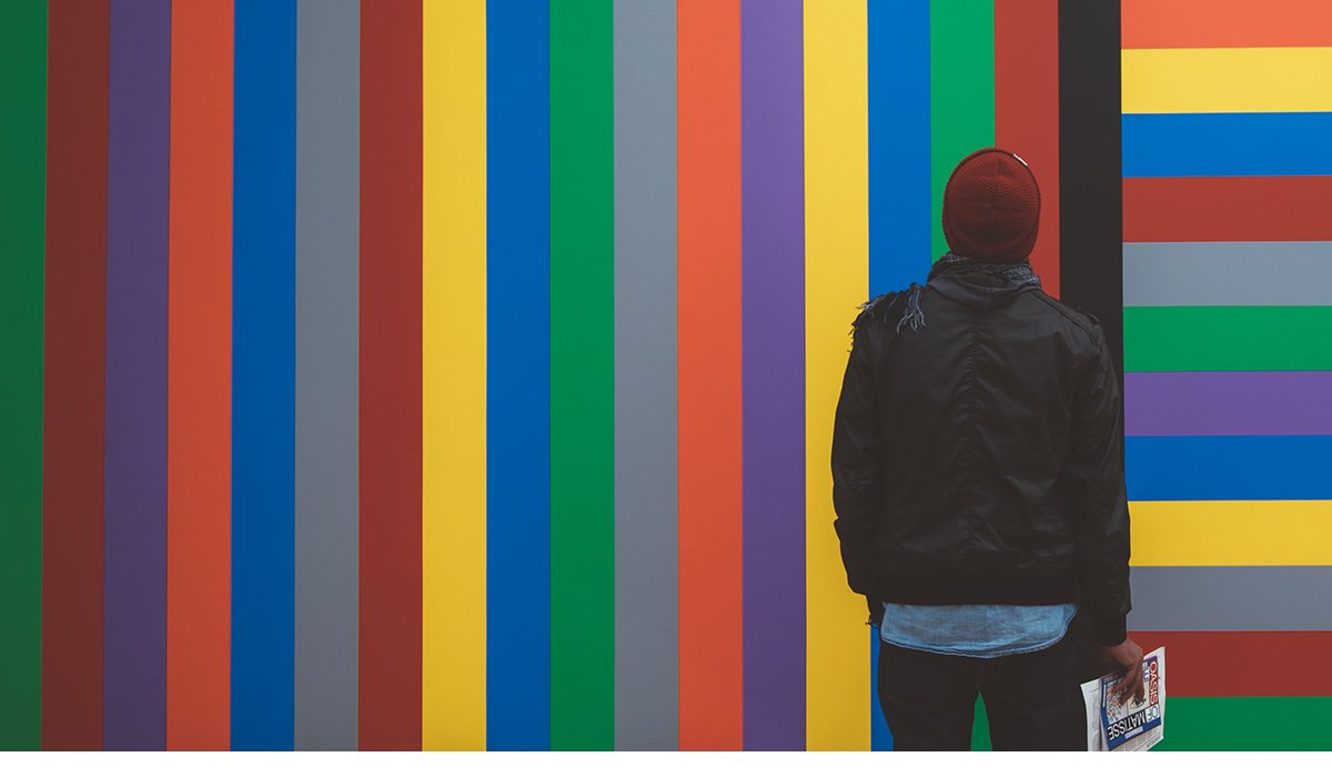 A person standing with her back towards us wearing a red cap in front of a striped wall 