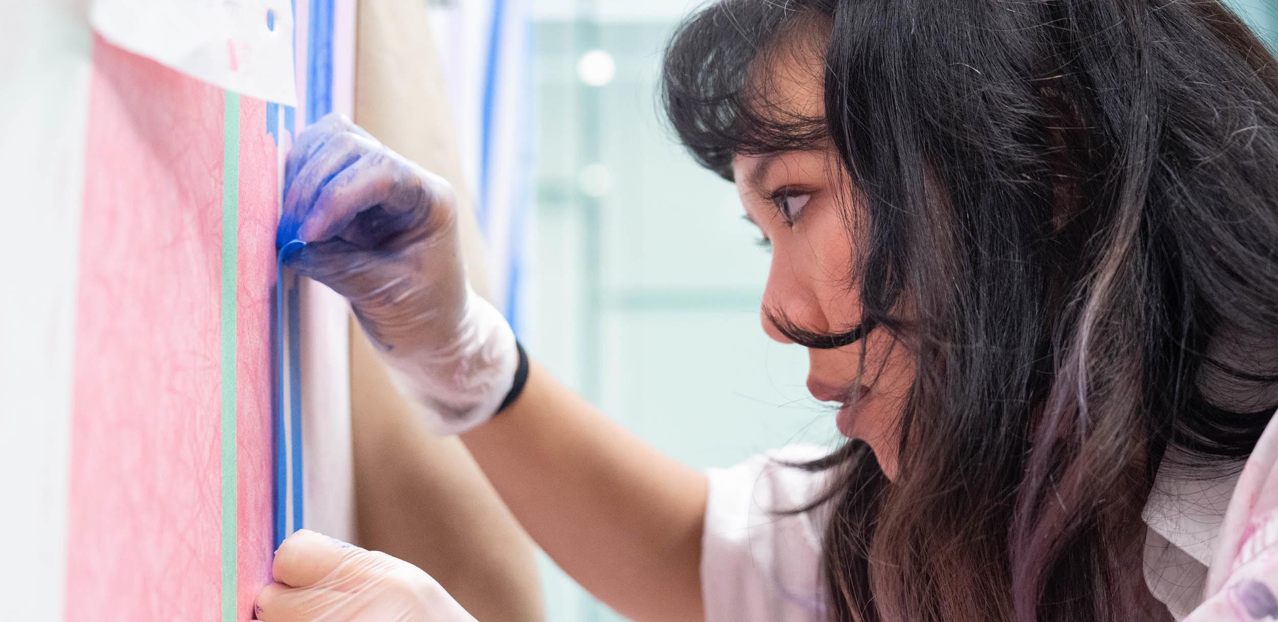 A profile shot of Nita Wareechatchai shows the recent graduate peeling tape off of the mural. 