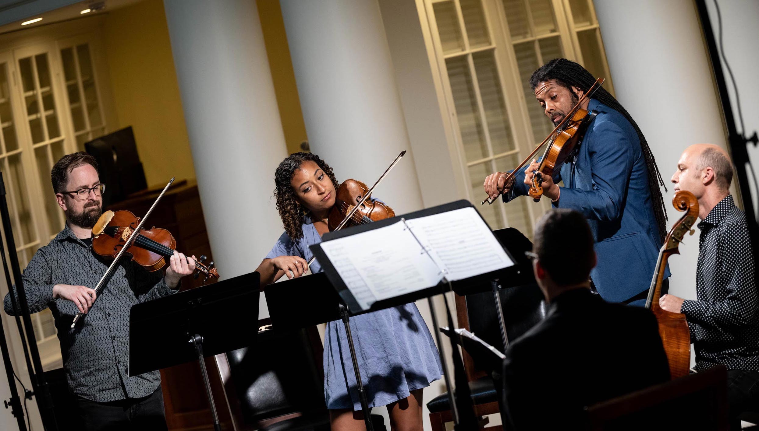 Three musicians read sheet music and play the violin and the fiddle. Another musician plays a bass viol.