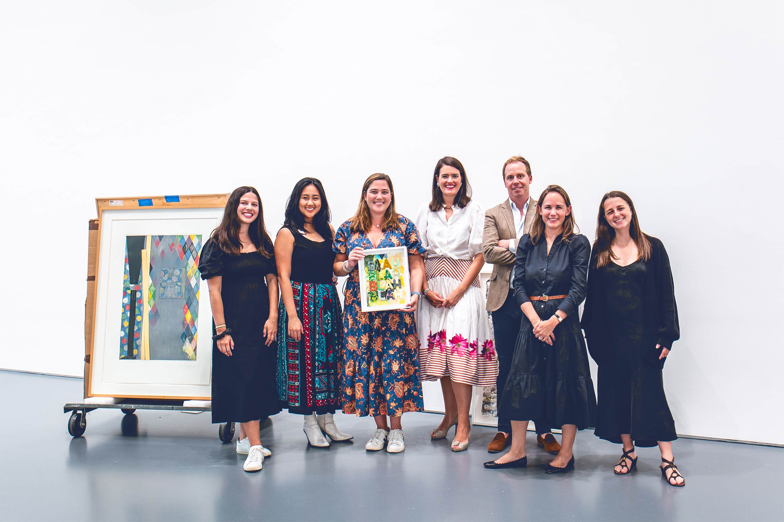 A group of well-dressed UVA alumni and Sotheby's employees pose with a piece of art work that includes the words "Blah blah blah blah".  