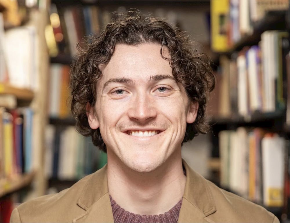 William Dozier smiles at the camera in front of rows of bookshelves.