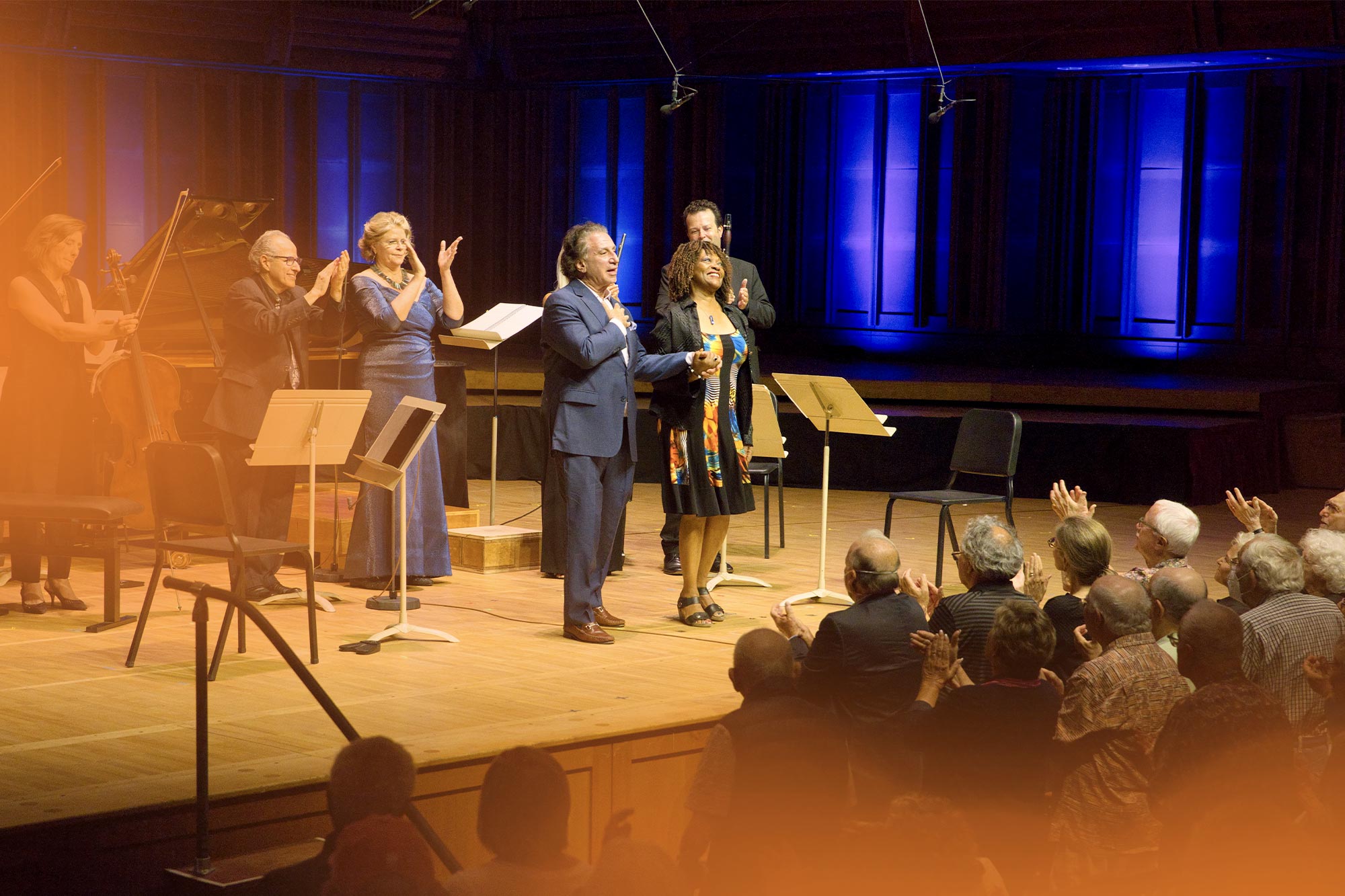 Professor Rita Dove and composer Richard Danielpour stand smiling on a stage, backed by several musicians. 