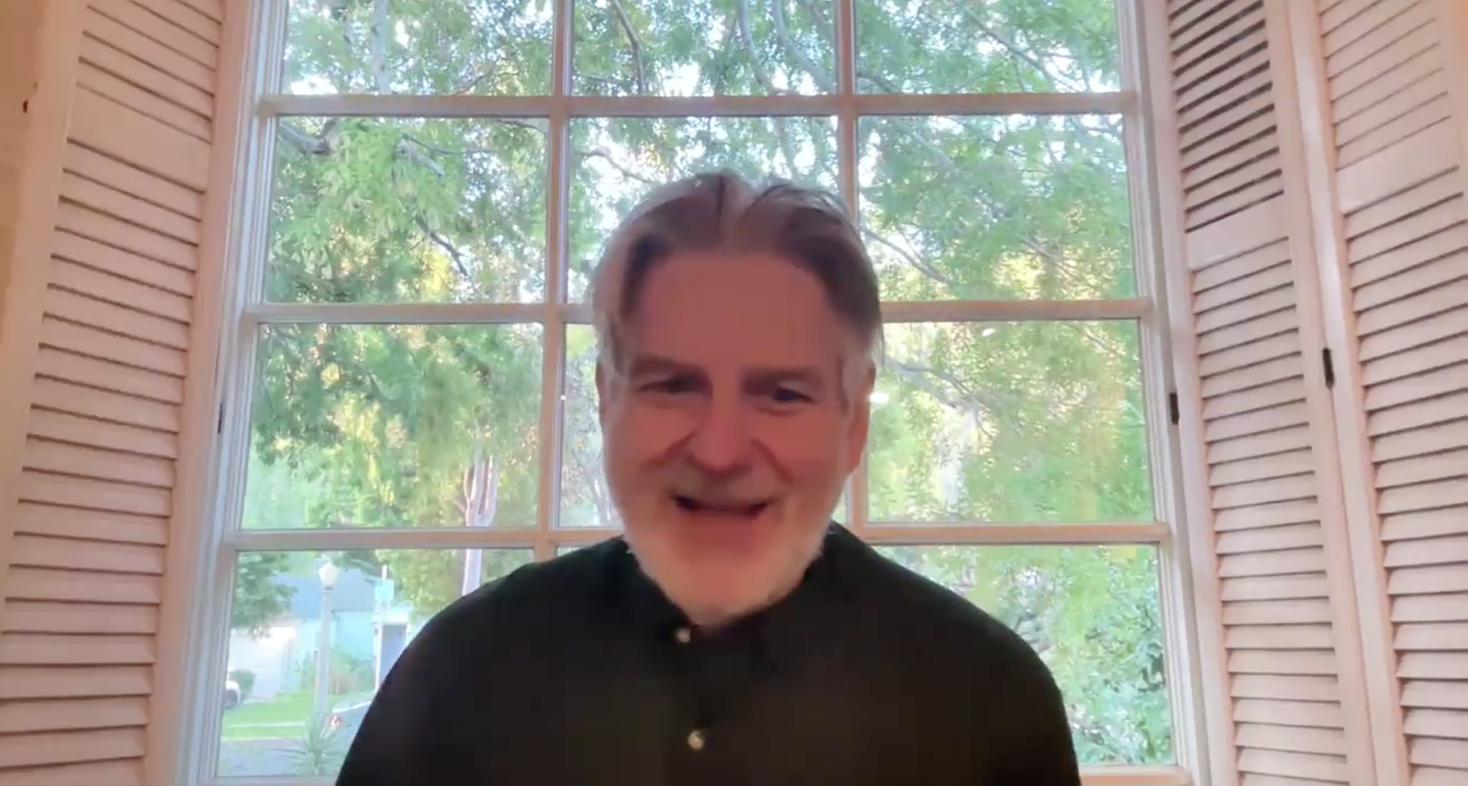 Peter Gould smiles and sits in front of a large window during a zoom call.