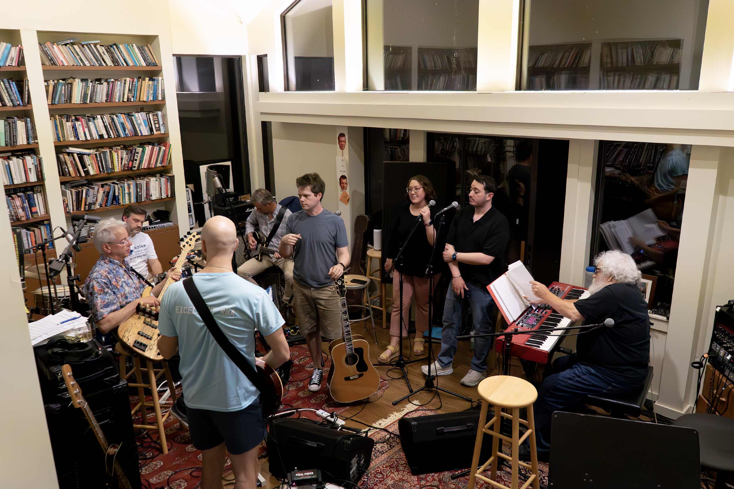 Blues Jam, consisting of eight members, play various instruments including guitars, a bass, and drums in an indoor space.