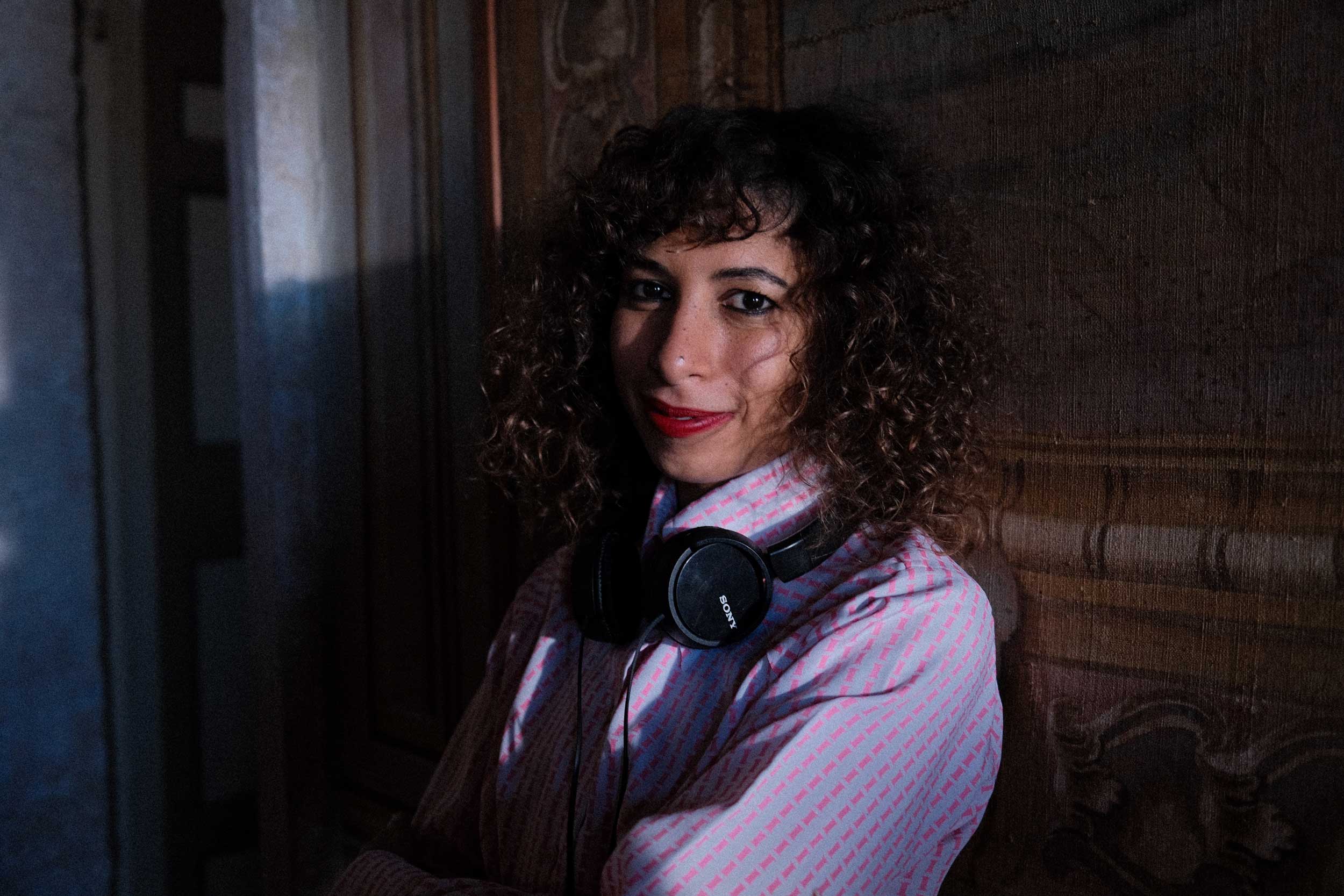 Hala Matar, wearing a blue-and-pink patterned shirt and headphones around her neck, smiles at the camera.