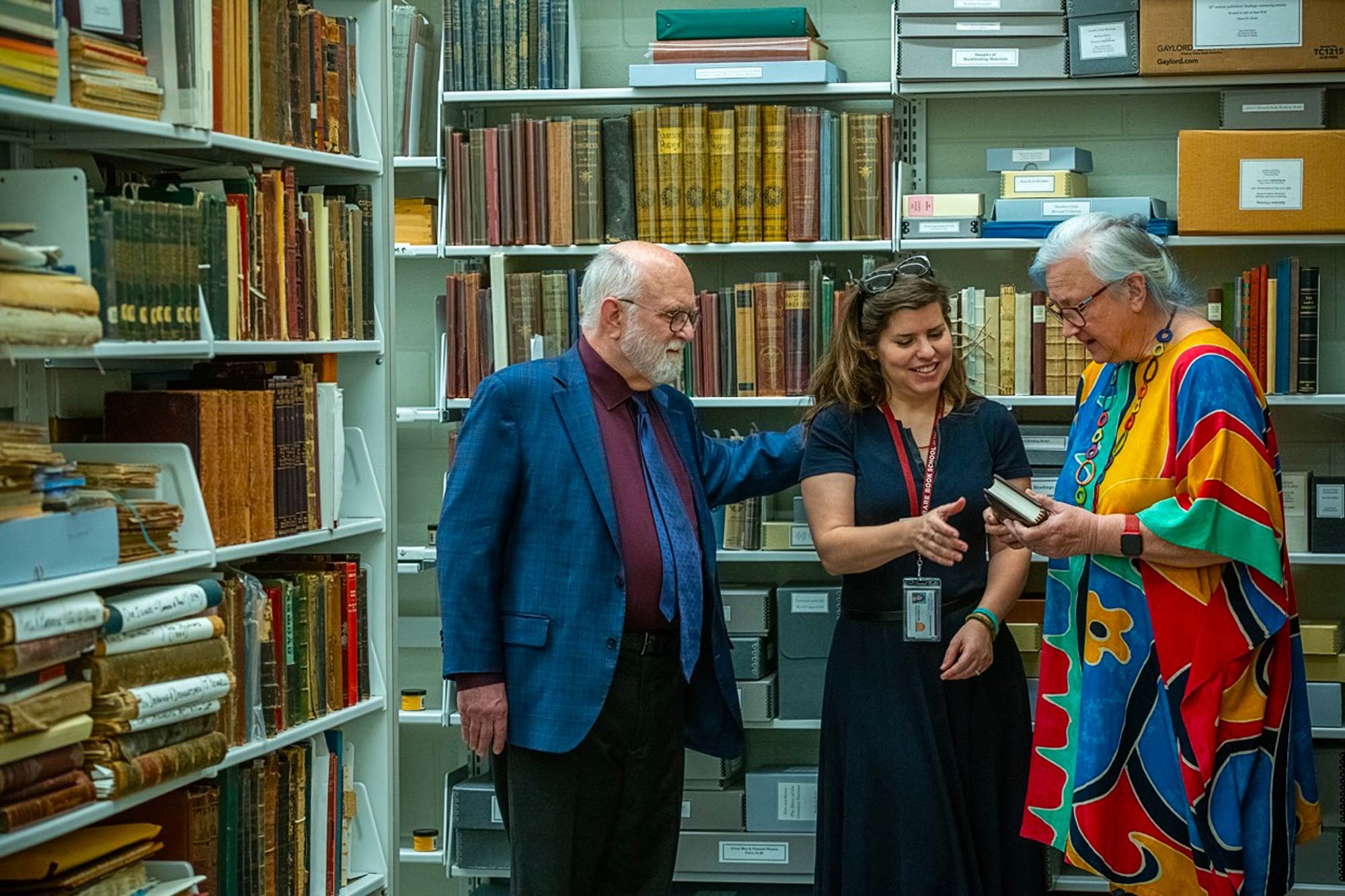 Glen and Cathy Miranker stand in a room full of book shelves with a librarian.