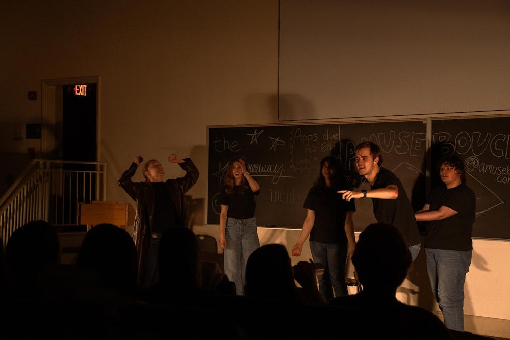 Five performers dressed in black act in a classroom in front of an audience.