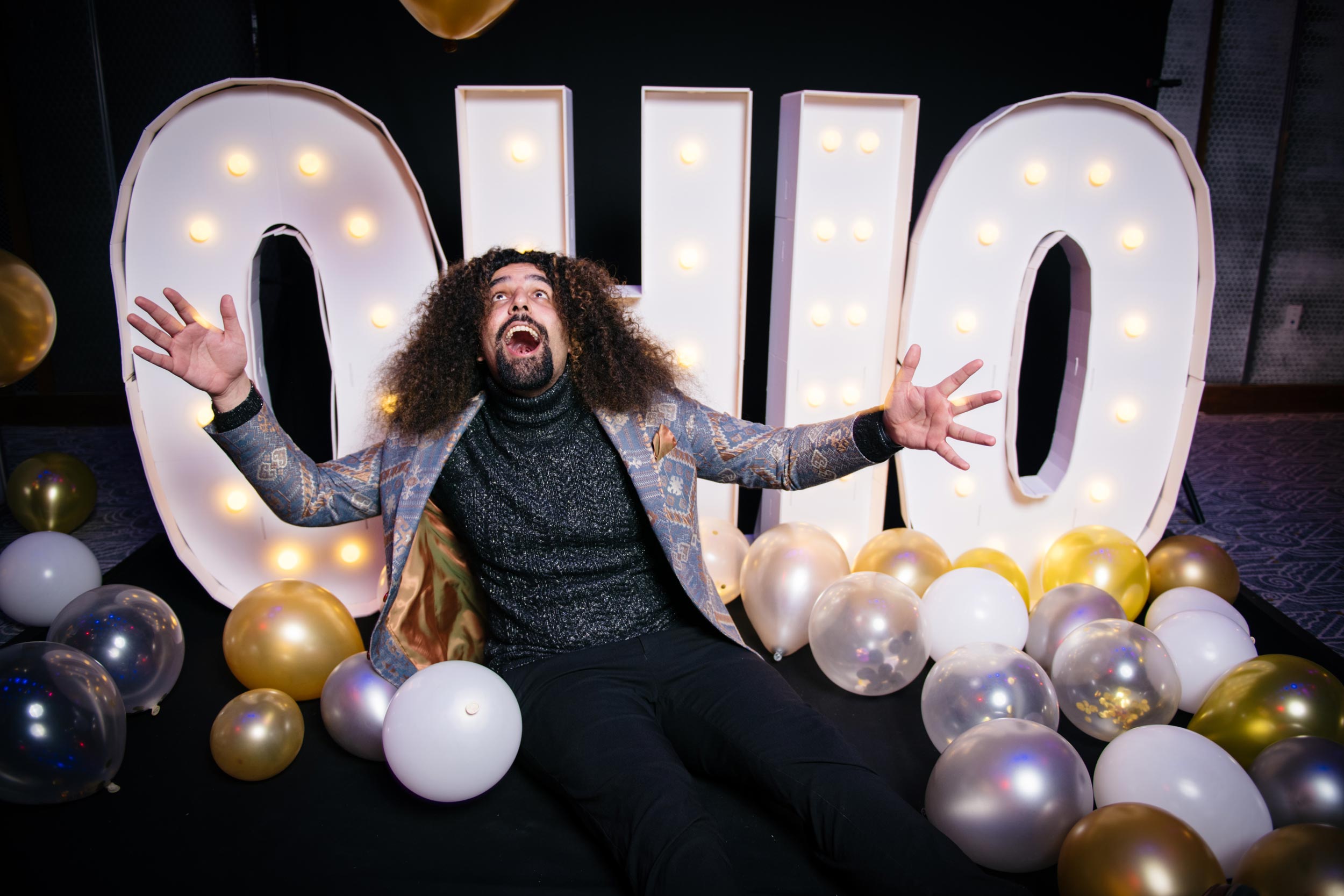 Anant Das strikes a comical pose in front of lit-up white letters that spell out "OHIO," surrounded by balloons.