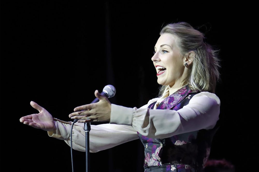 Jenna Pastusek sings into a microphone, extending her arms out towards the crowd.