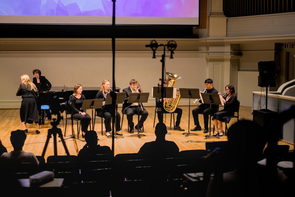 Six student musicians sit on stage with their music stands and instruments during a performance.