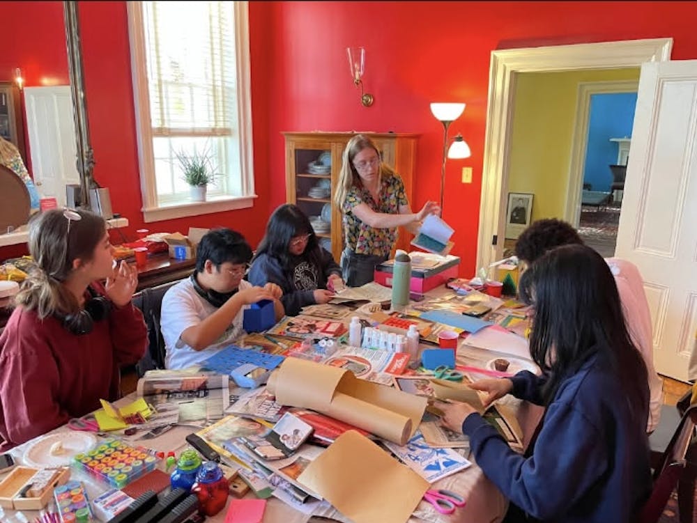 A picture of the student event where visitors are seen creating zines at a table, which is covered in various colorful art supplies.