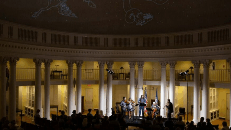 Photo of the inside of the Rotunda with a small group of musicians playing string instruments in front of an audience. 