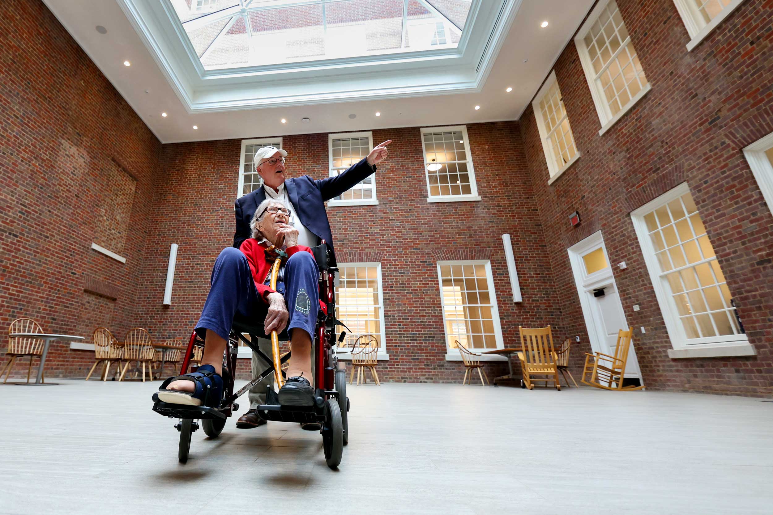 Mary Catherine Dunnigan is given a tour of Shannon library while in a wheelchair, and a man points out areas in the room while pushing her chair.