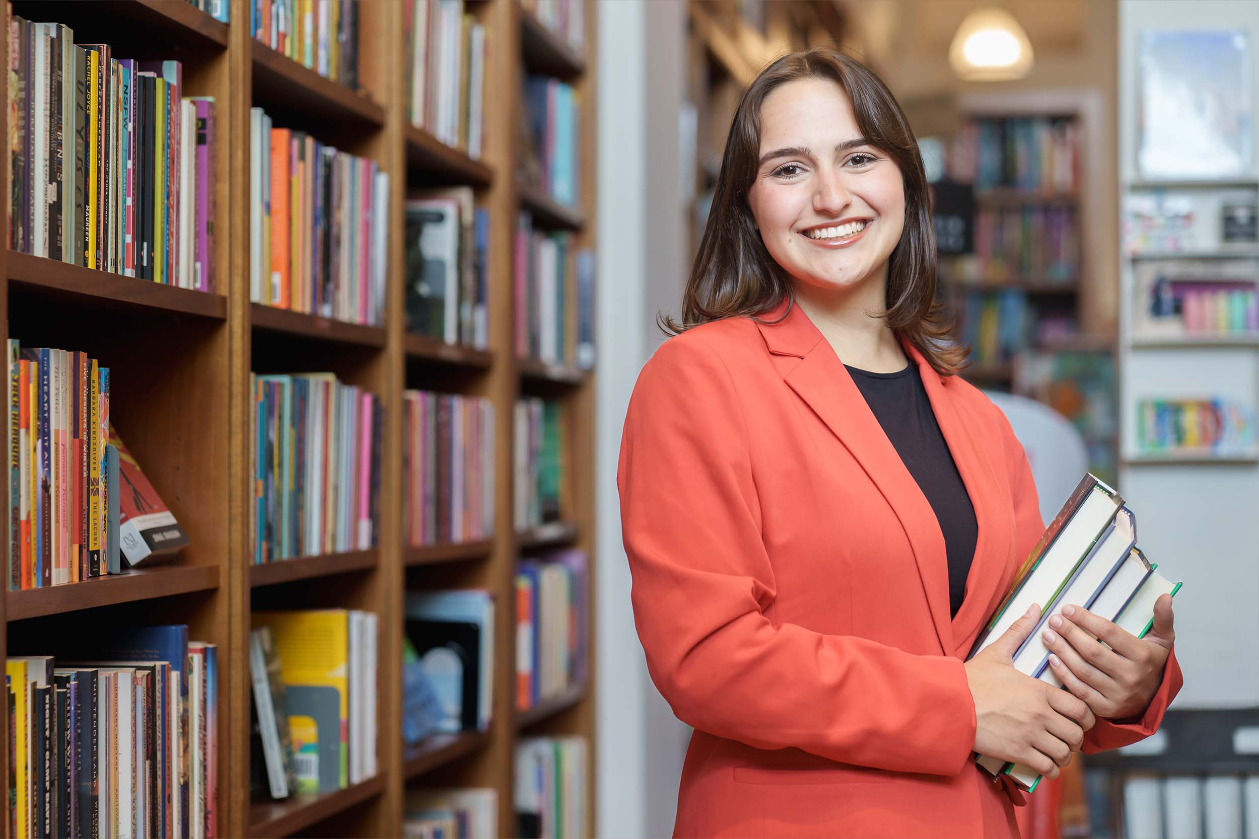 Molly Rathbun poses at New Dominion Bookstore, holding a stack of books.