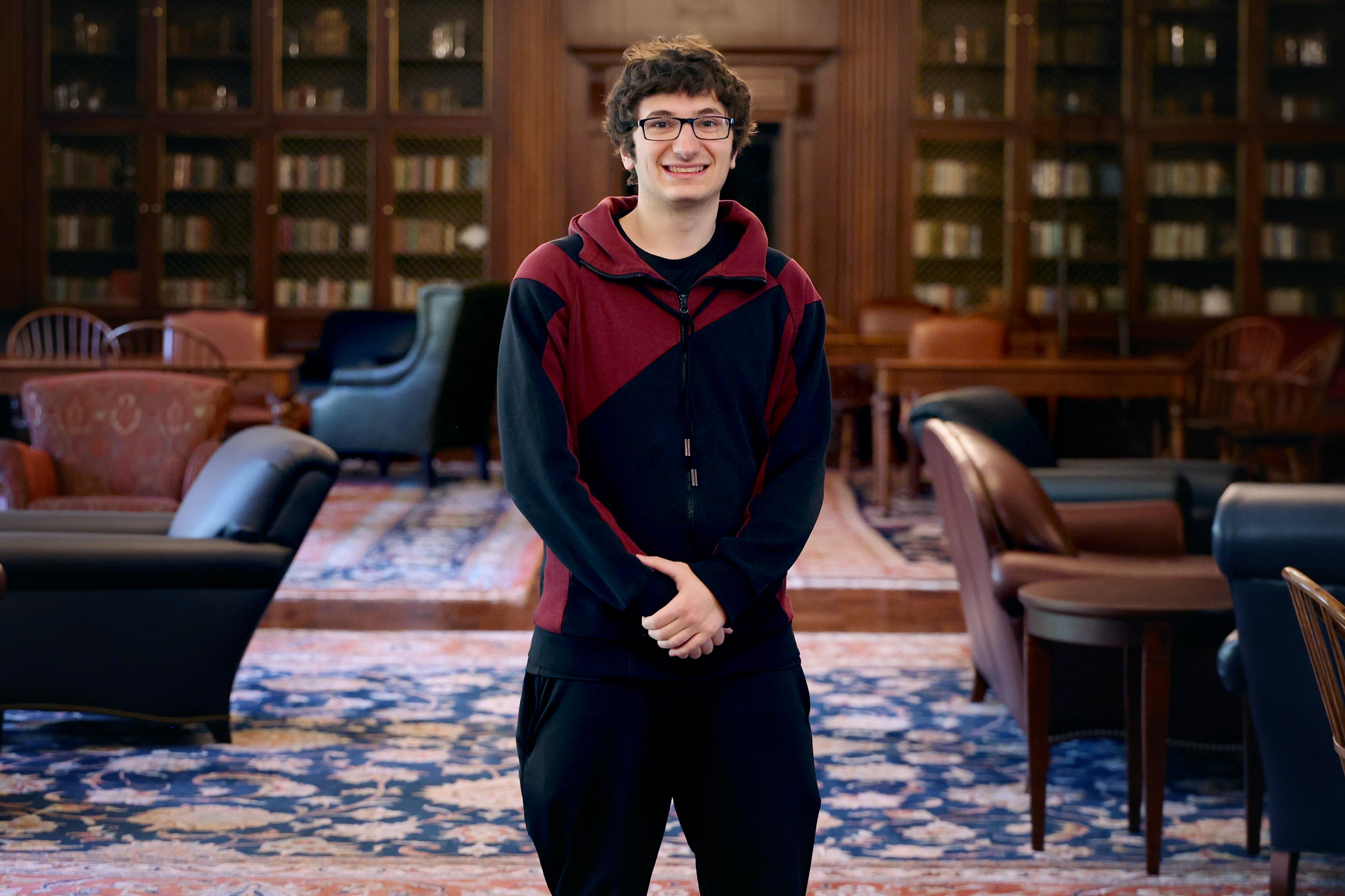 A picture of UVA student Tyler Ruvolo standing in Shannon Library surrounded by bookshelves.