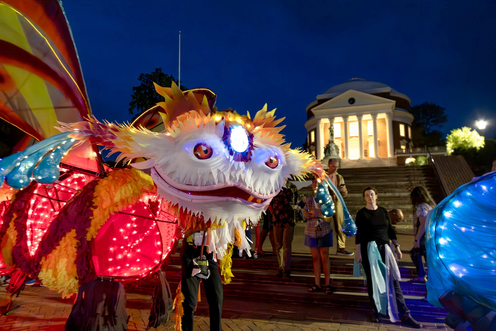 A colorful puppet creature is shown in front of the Rotunda at night.