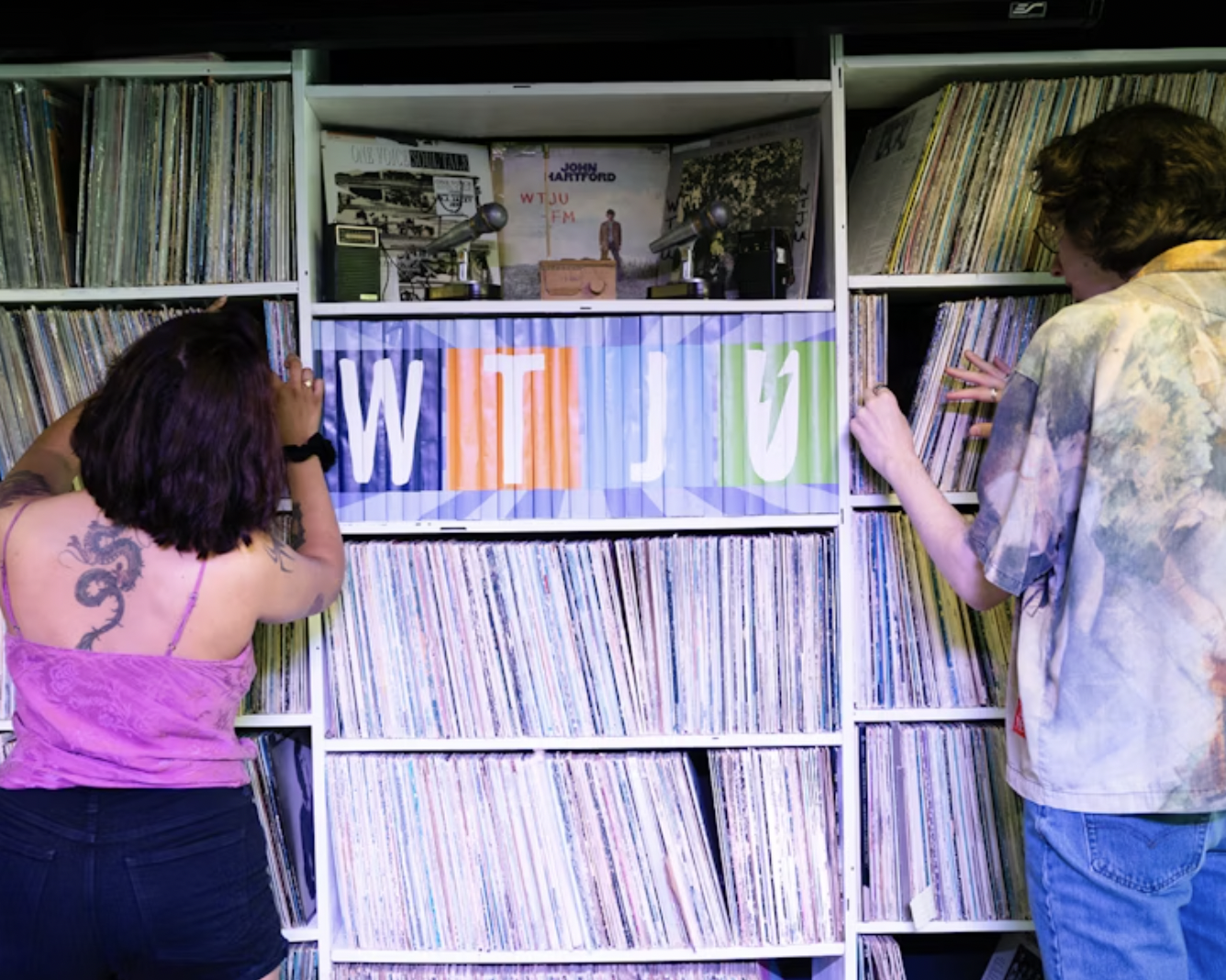 An image of two students browsing records on shelves with the label WTJU showcased on the center shelf.