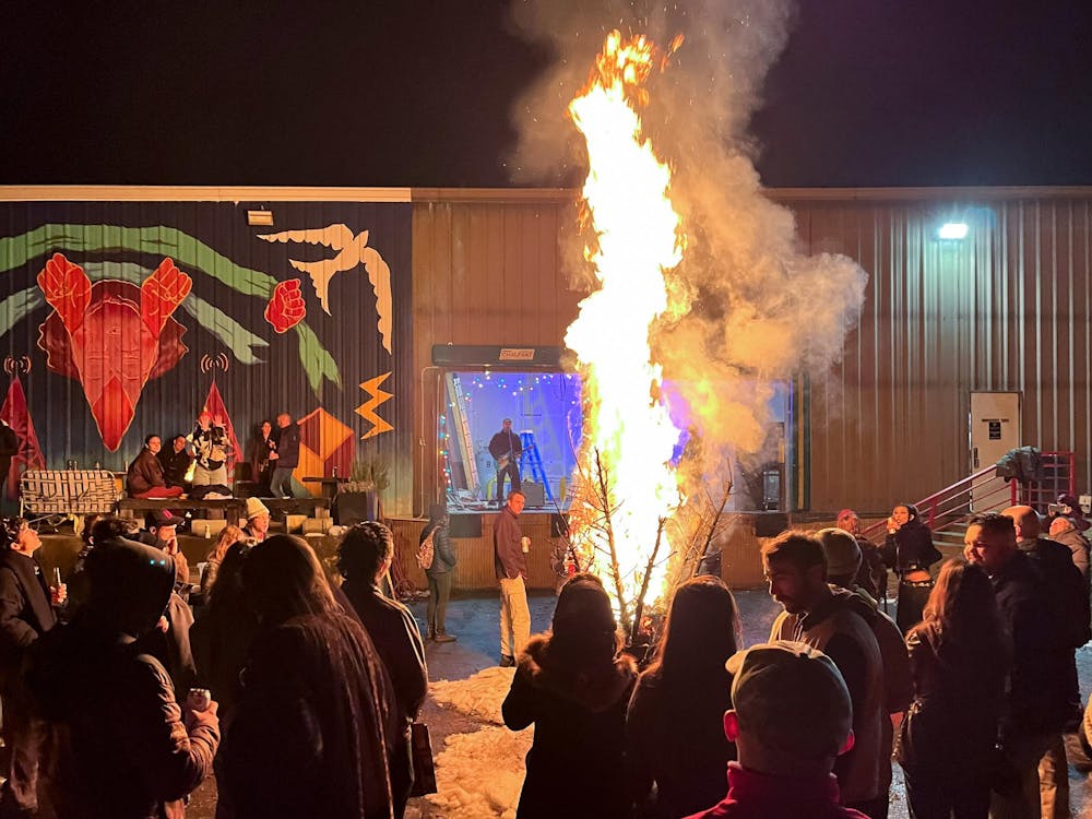 A picture of a Visible Records event, where people are gathered outside at night in front of a bonfire.