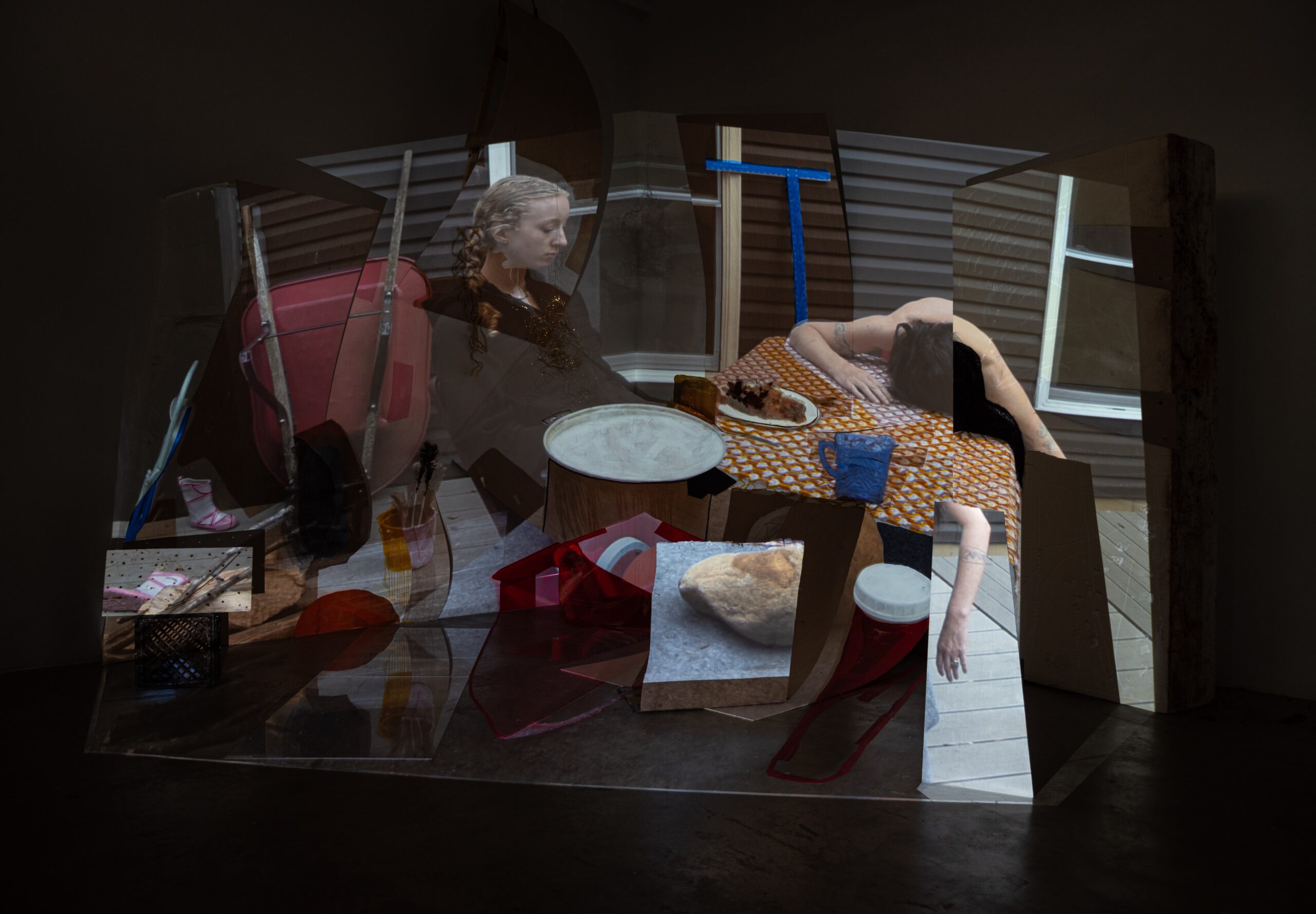 A picture of the installation at Visible Records. It is a projection of a woman surrounded by household objects, and it is projected onto various 3D white objects.