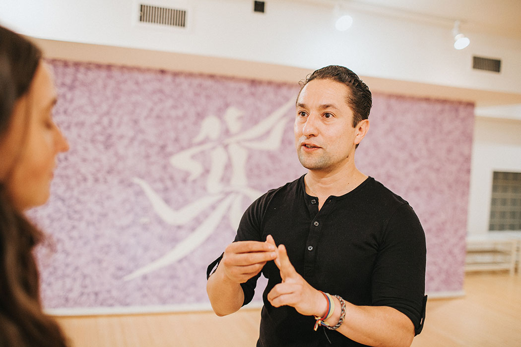 A picture of Edwin Roa instructing a woman while standing in a brightly lit dance studio, wearing a black shirt.