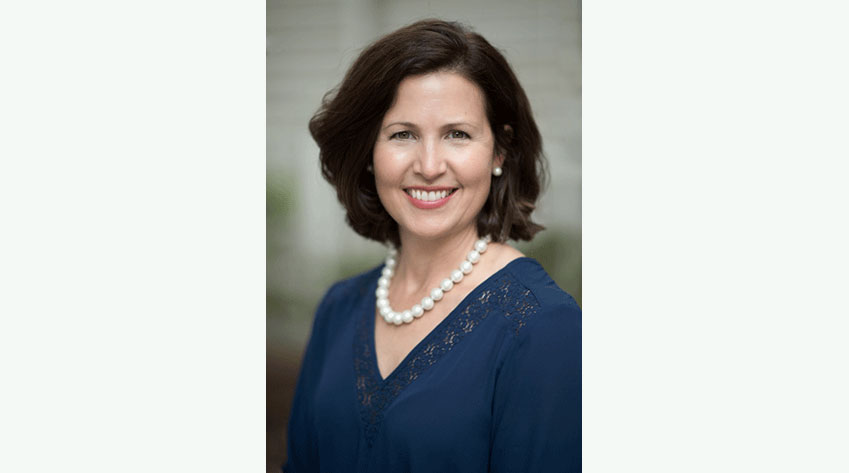 Headshot of Carolyn Keurajian in a blue blouse and a pearl necklace. She has dark brown hair that ends at her shoulders.
