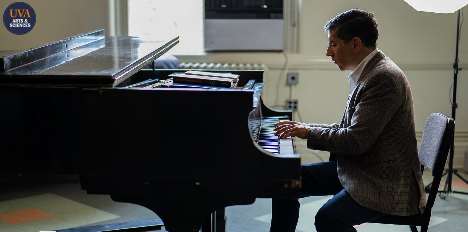 A profile image of a man in a suit sitting at a piano with his hands on the keys.