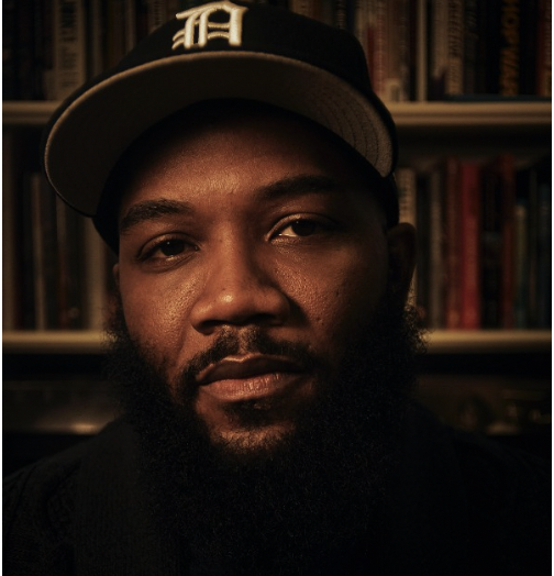 Close-up photo of Dr. A.D. Carson wearing a black baseball hat, standing in front of a bookshelf.