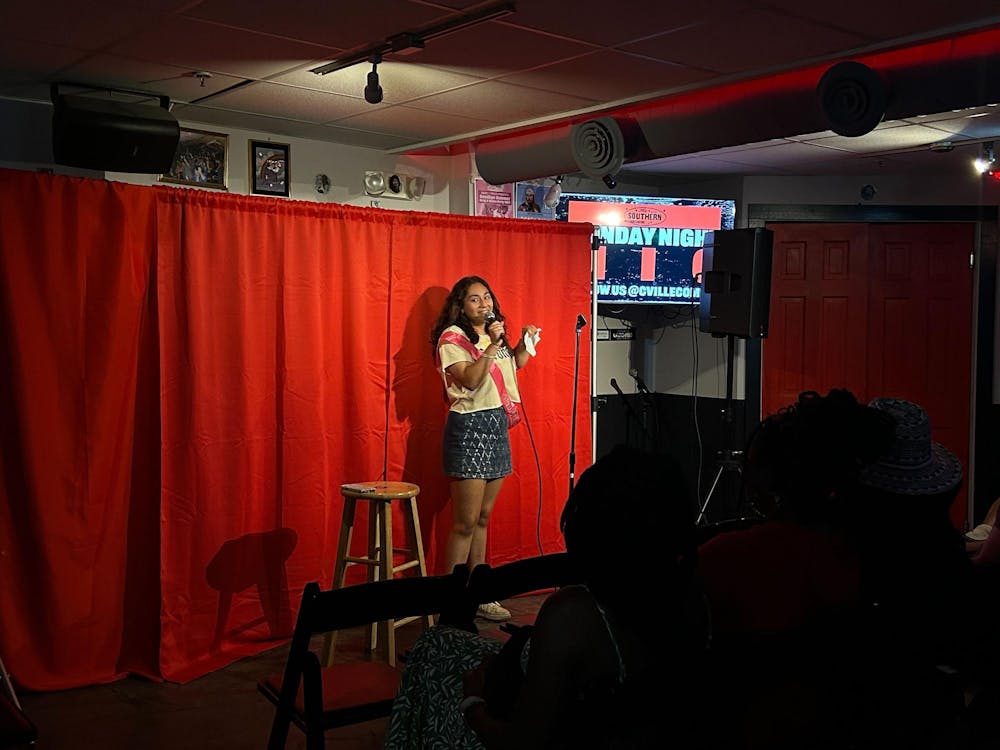 A fourth year UVA student stands in front of a bright red curtain with a wooden stool and is talking into a microphone.