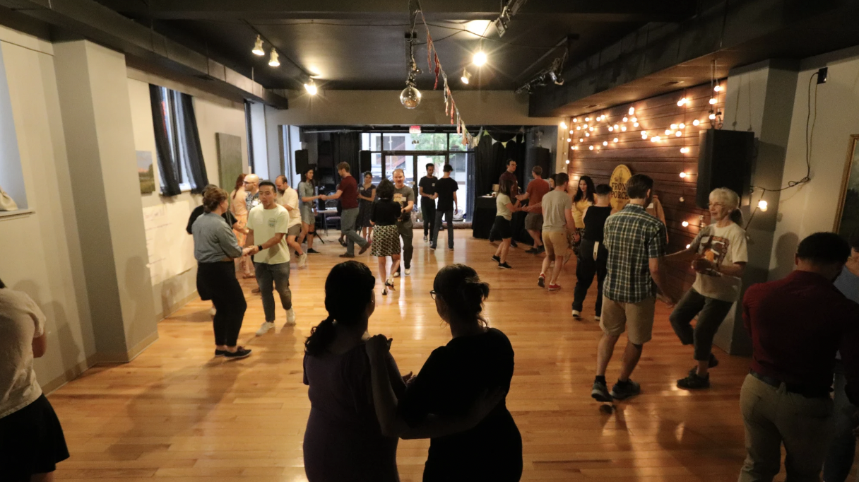A room wood floors and string lights filled with couples swing dancing in casual clothes.