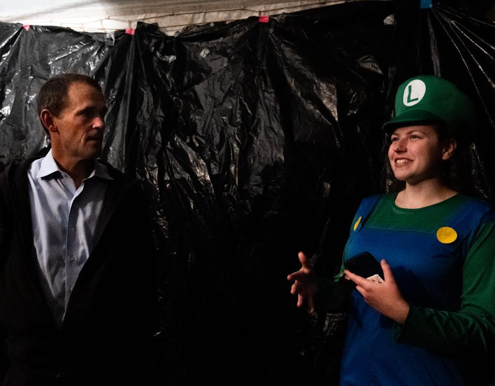 Jim Ryan stands in a dark room with a student dressed up in a Luigi Halloween costume for the Brown College Haunted House.