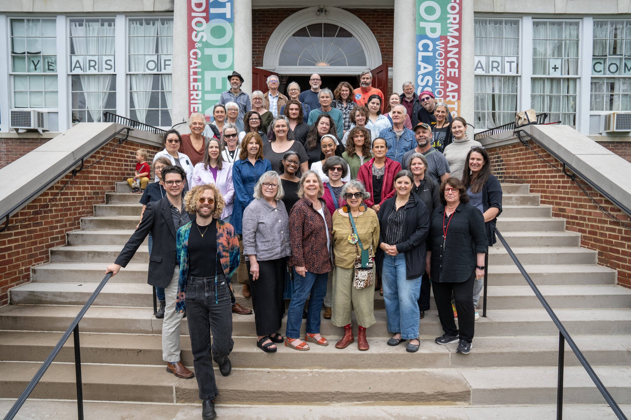 A large group of artists stands outside on the steps of a large building.