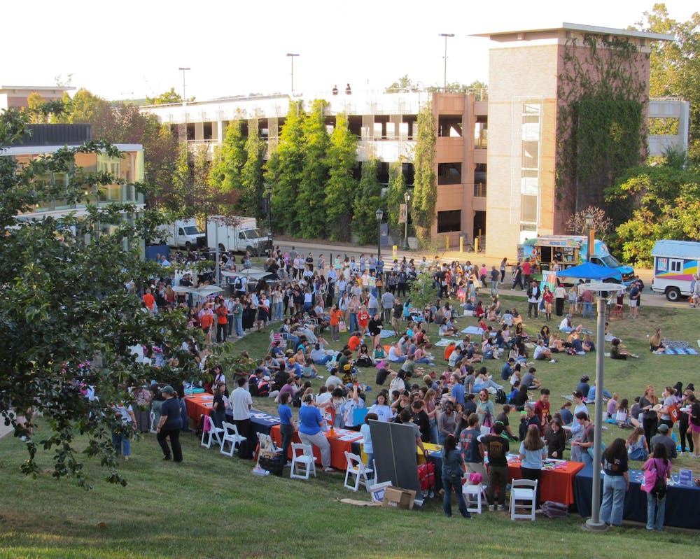 A distant image of the field outside the Drama Education building filled with students and faculty, sitting and working at tables, advertising for arts organizations.