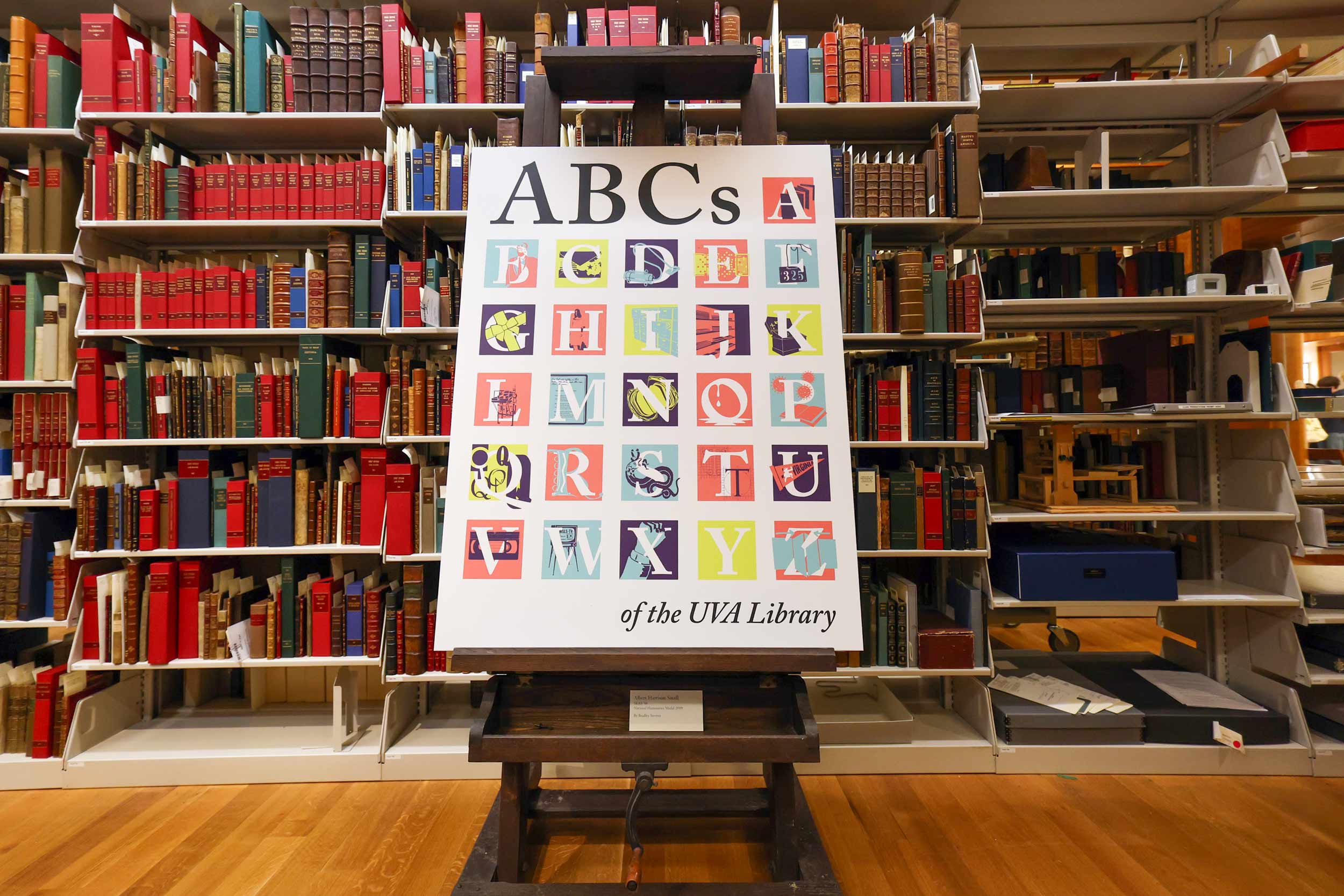 A poster board with the colorful letters of the alphabet is propped up in front of a bookshelf filled with books.