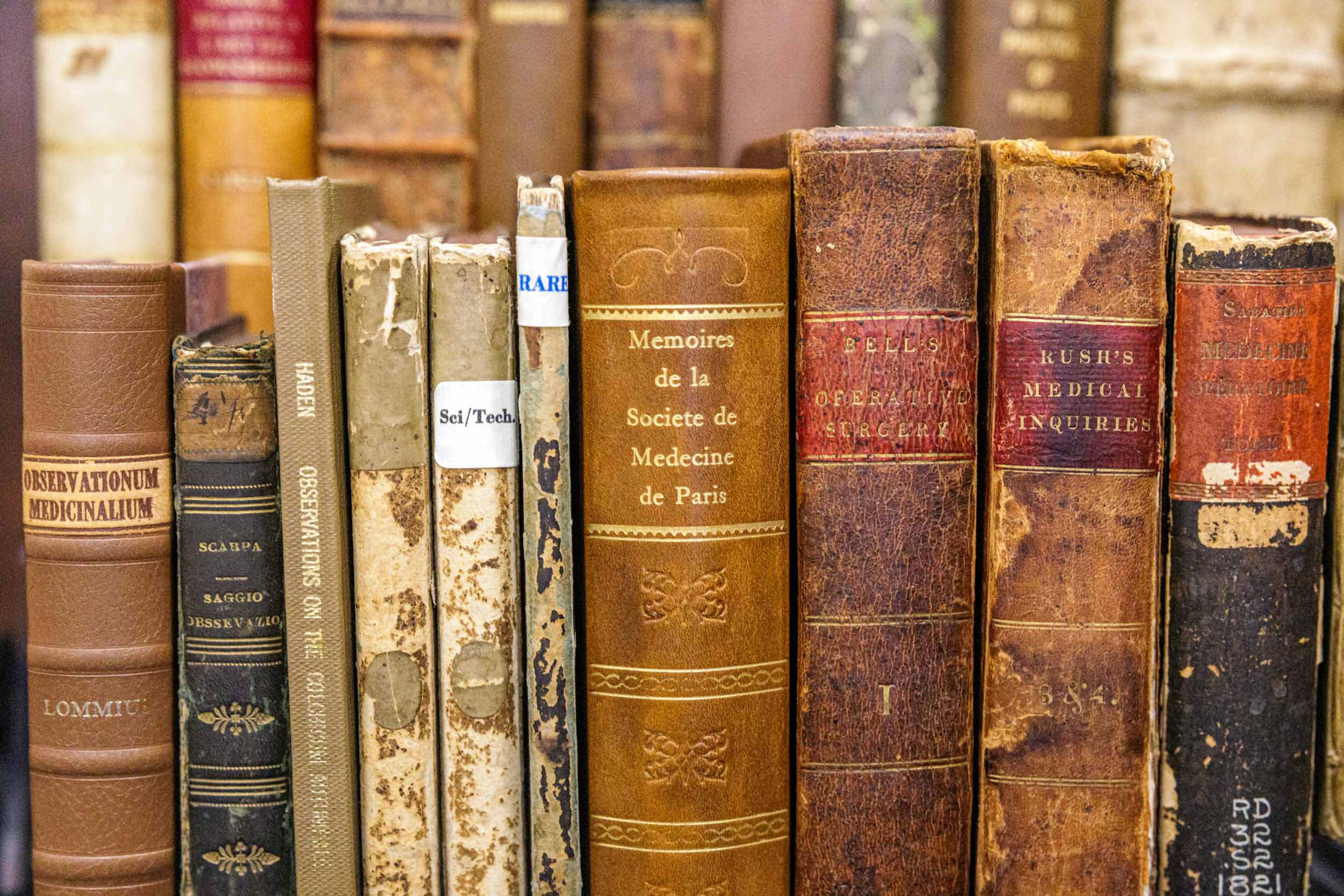 A close up image of old books, the spines are tattered and most are brown colored.