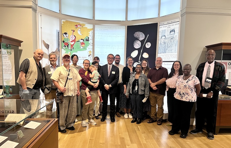A group of around 15 people stand in a semi-circle in front of a display of wall art.