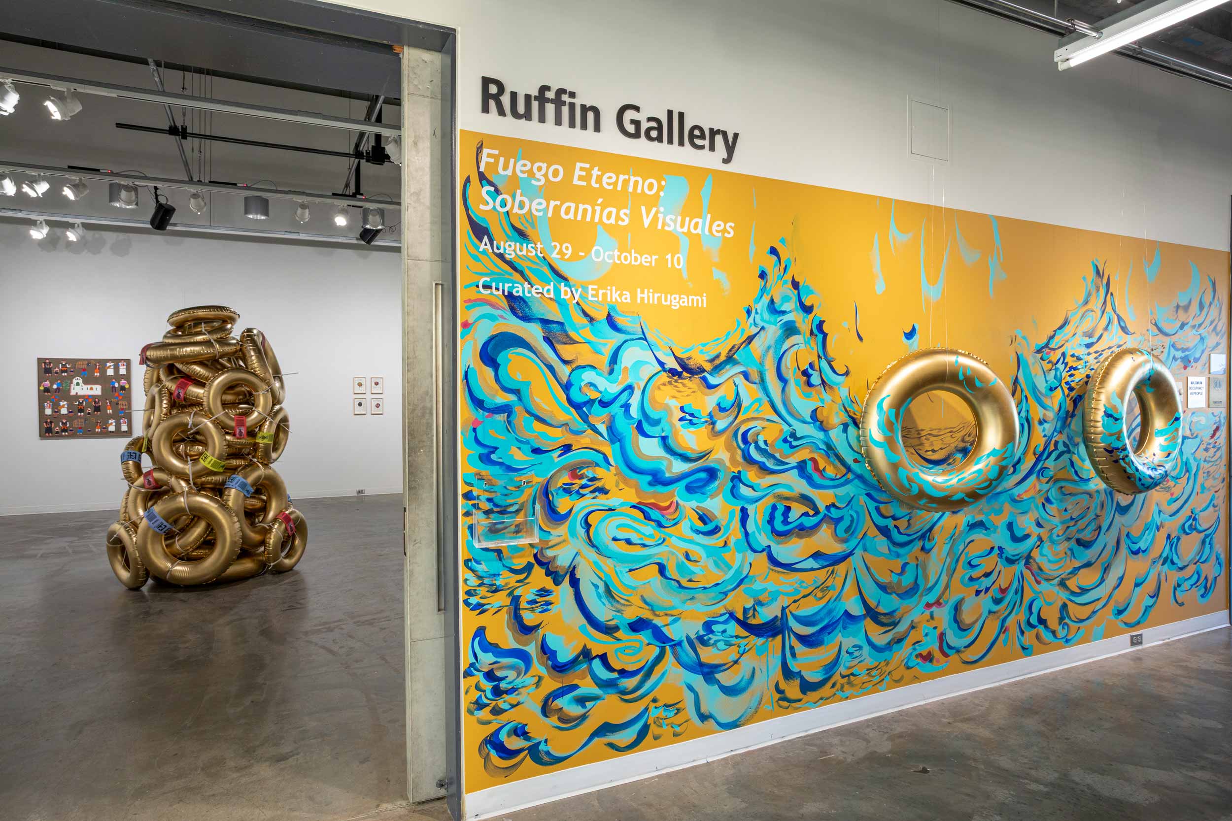A wall in the UVA Ruffin Gallery is painted with a ocean wave-like pattern and has inner-tubes hanging in from of the wall, also painted with a wave pattern. 