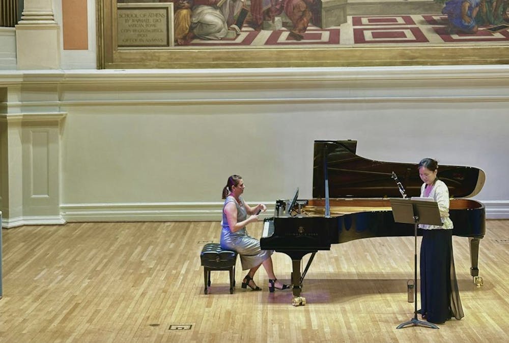 The bright stage in Old Cabell with a performer at a music stand and another performer sitting at a grand piano.