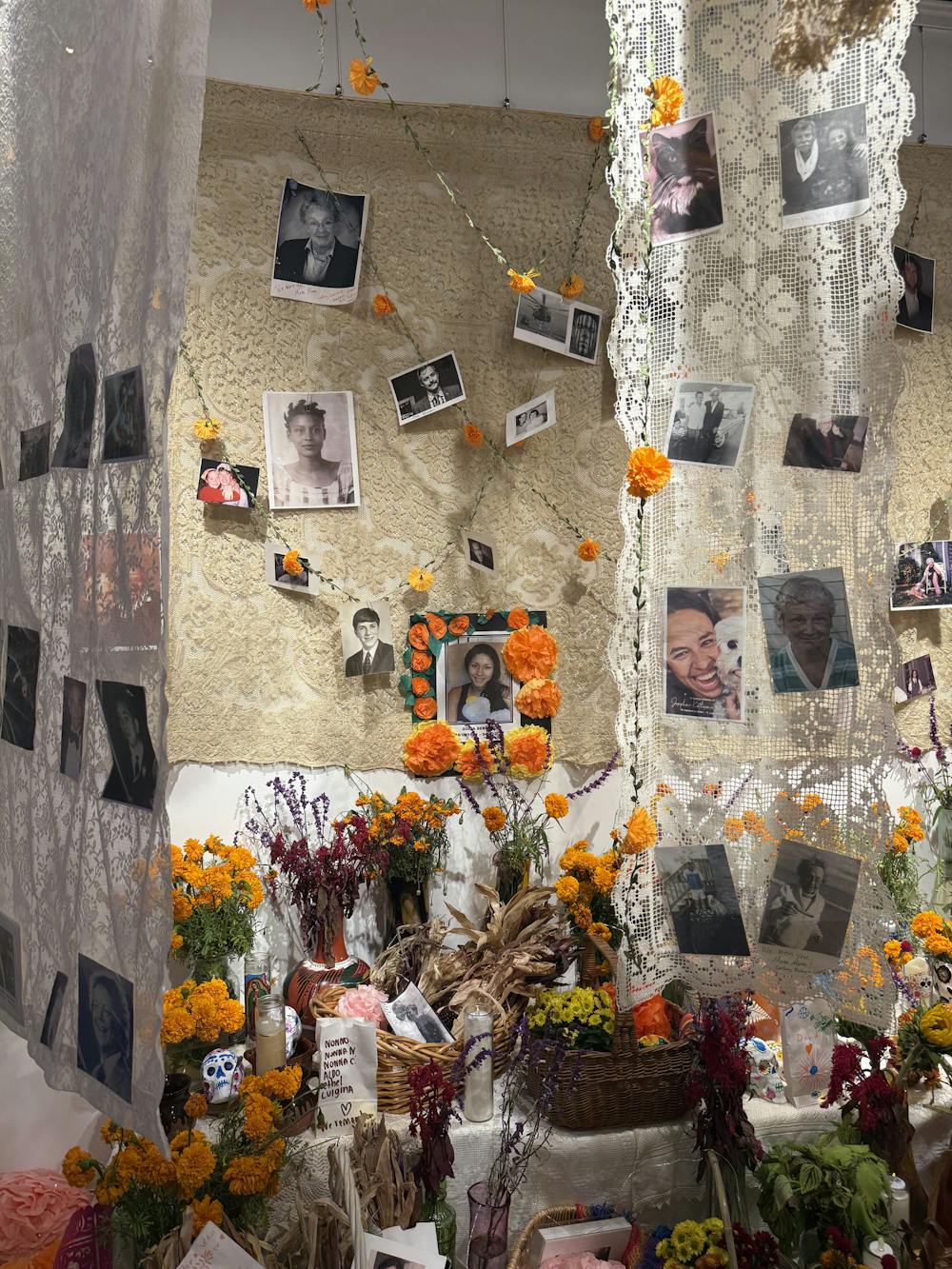 A display of lace fabrics, black and white photos, and garlands of yellow marigolds, with a collection of flowers in vases and bouquets bellow the images.