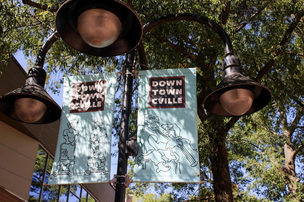 A close up of the top of a lamppost with two light blue banner signs saying "Downtown Cville."