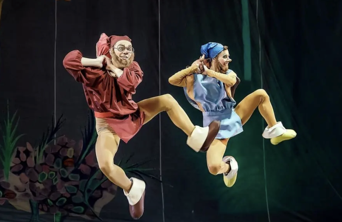 Two male ballet dancers are in Snow White Dwarf costumes and are jumping to click their heels.