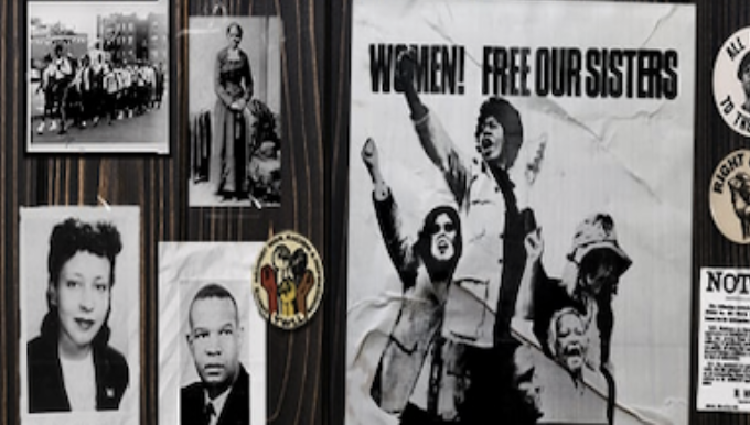 A bulletin board with various black and white photos of Black women, some posters related to fighting for justice. One reads, "Women! Free Our Sisters!"