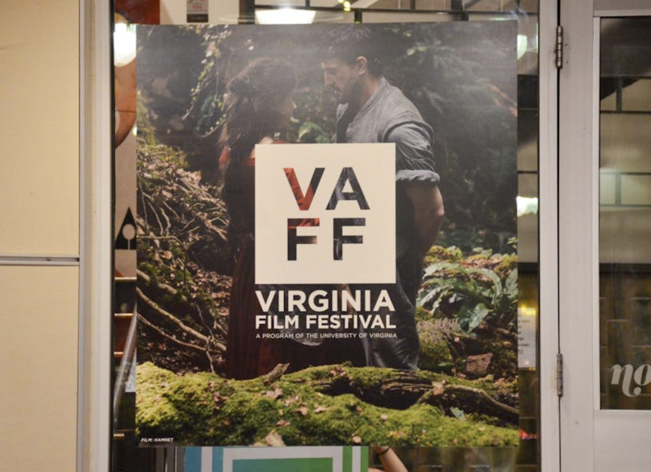 A glass door with a film poster taped to the surface. The image on the poster is of a man and a woman standing close together, in the middle of the woods. In the center of the poster is a white VAFF logo in a square.