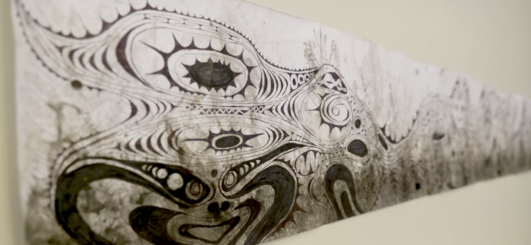 A long white paper with abstract black ink designs, displayed on a white wall.