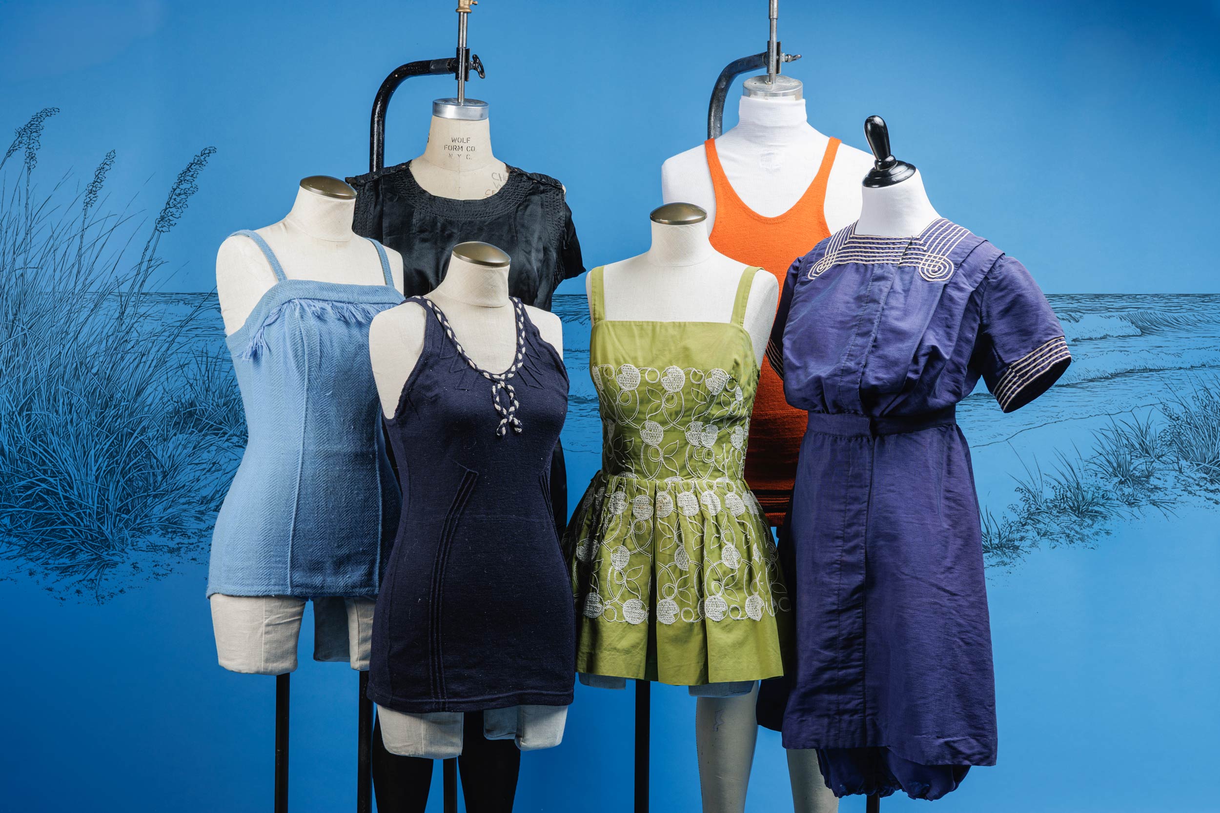 A muted background of a drawn beach scene. In front, 6 mannequins showcase different styles and colors of vintage beach swimwear from years past.