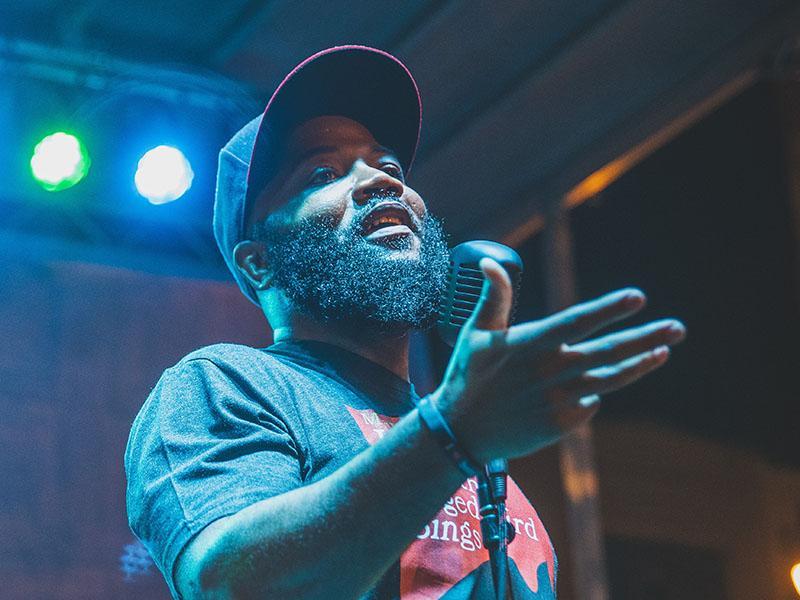 A picture of Dr. A.D. Carson standing at a microphone with blue and green lights shining from behind him.