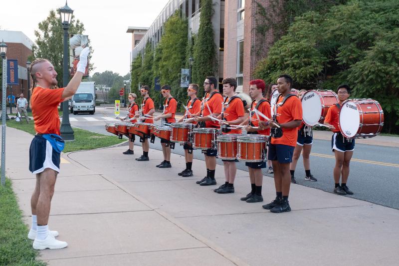 The Cavalier Marching Band stands in a drumline while being conducted. 